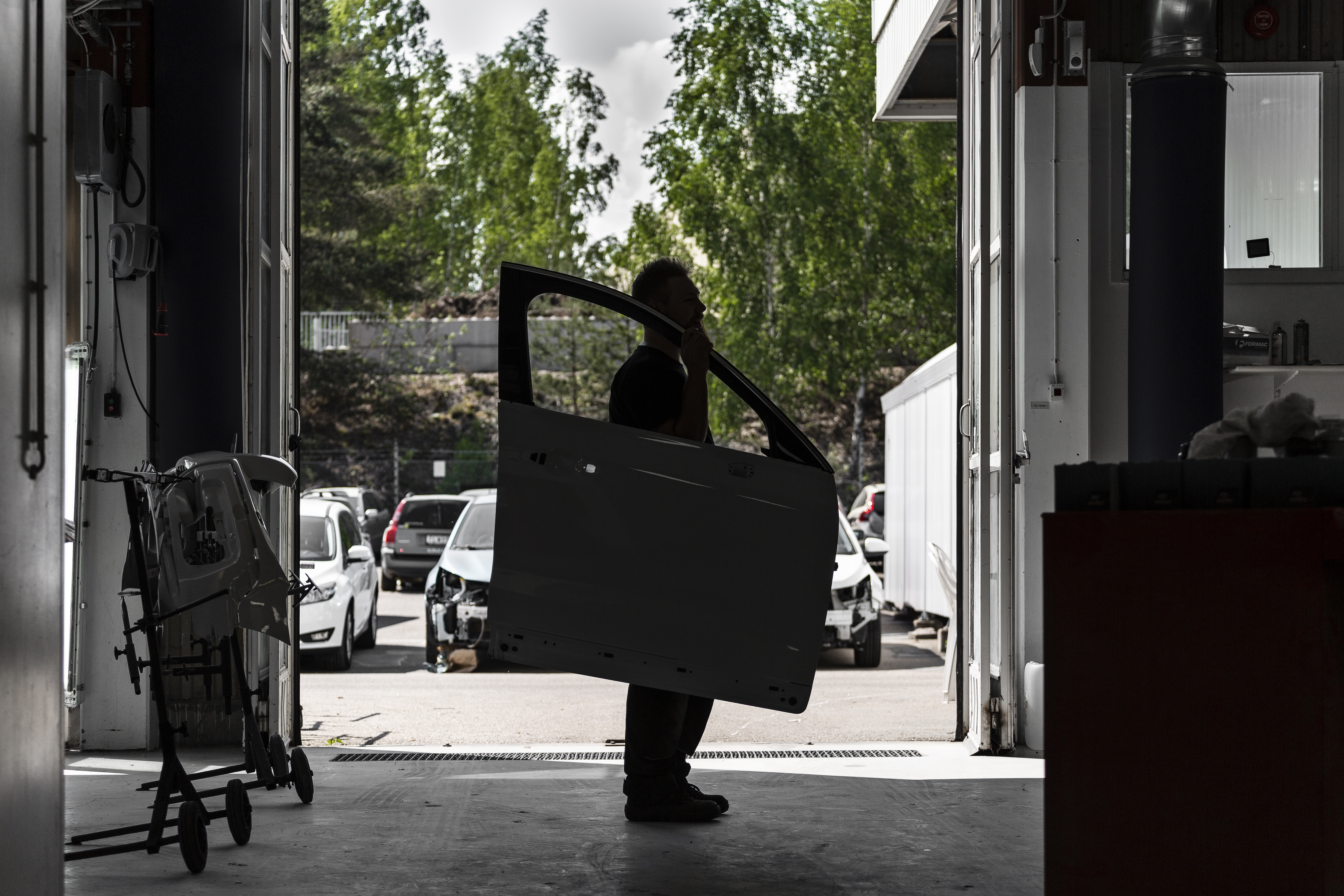 En mörk siluett av en skadetekniker som bär på en bildörr. I bakgrunden syns några demonterade bilar.